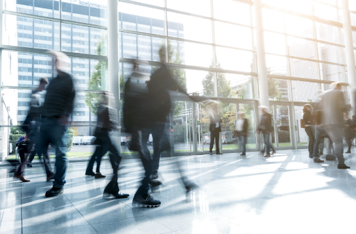 Decorative image of people walking in a sun lit glass office building